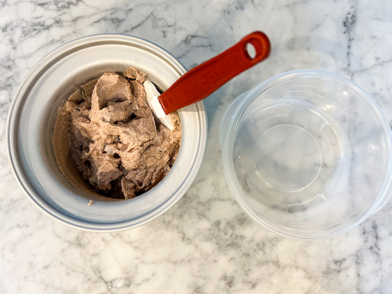 Ice cream maker with chocolate cherry ice cream, a spatula, and an empty plastic container