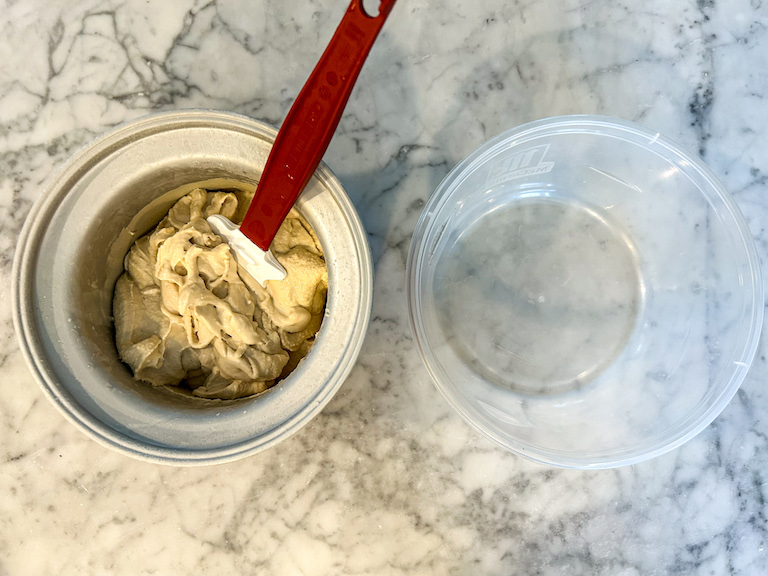Earl Grey tea ice cream in an ice cream maker with a spatula, on a marble countertop next to a plastic container