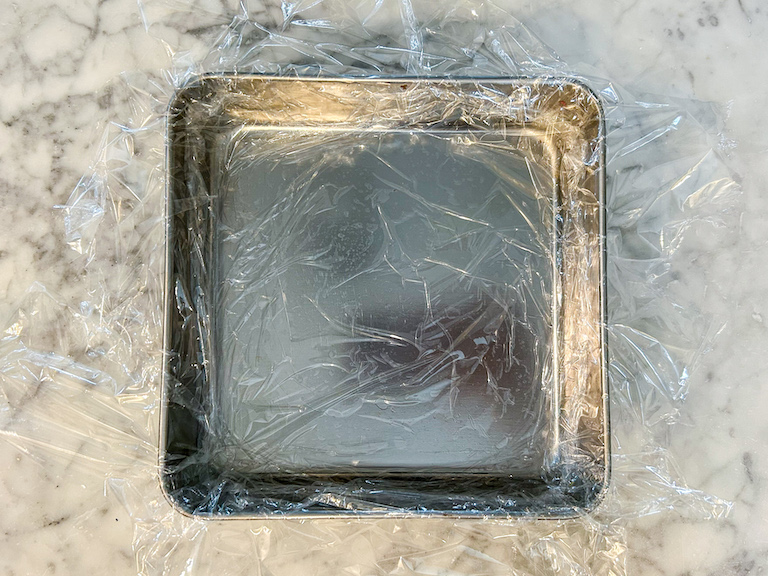 A square metal tin lined with clingfilm