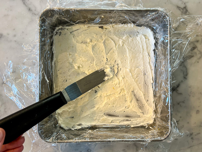 Small palette knife spreading cheesecake mixture into a metal tin