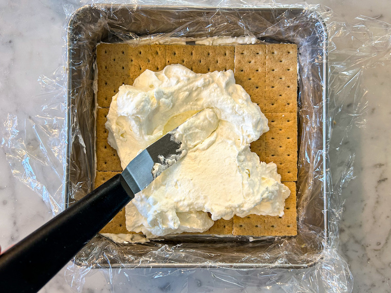 Palette knife spreading cheesecake filling over a layer of graham crackers