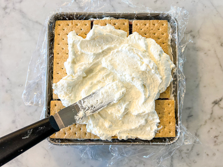 Palette knife spreading cream cheese filling over a layer of graham crackers