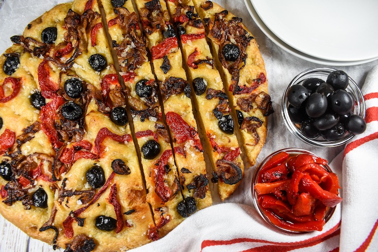 Horizontal shot of a loaf of caramelized onion and roasted red pepper focaccia with a red striped towel