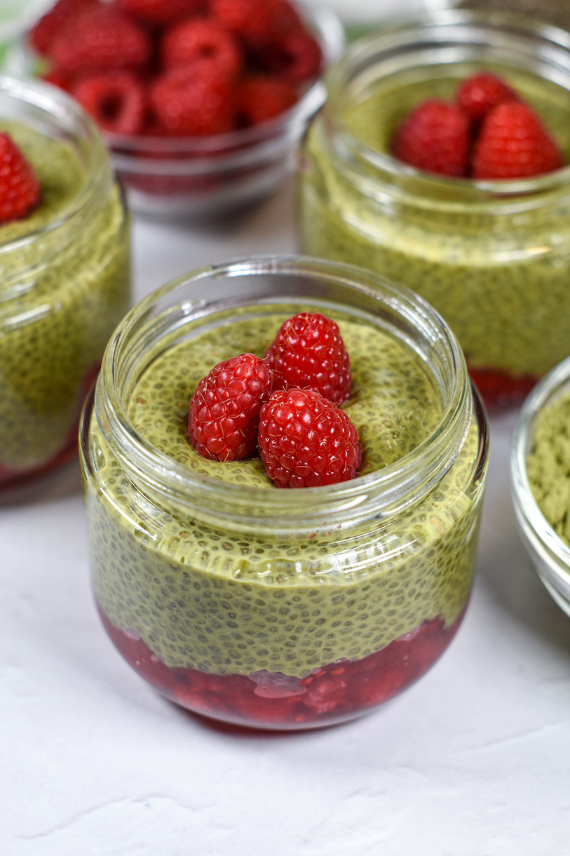 A jar of matcha chia pudding garnished with three red raspberries