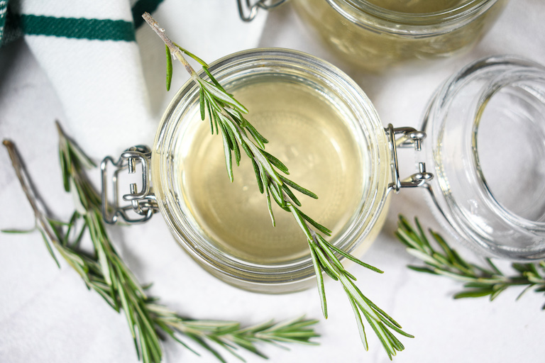 Looking down at a jar of rosemary syrup with a sprig of fresh rosemary on top