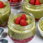 glass jar of matcha pudding garnished with fresh raspberries