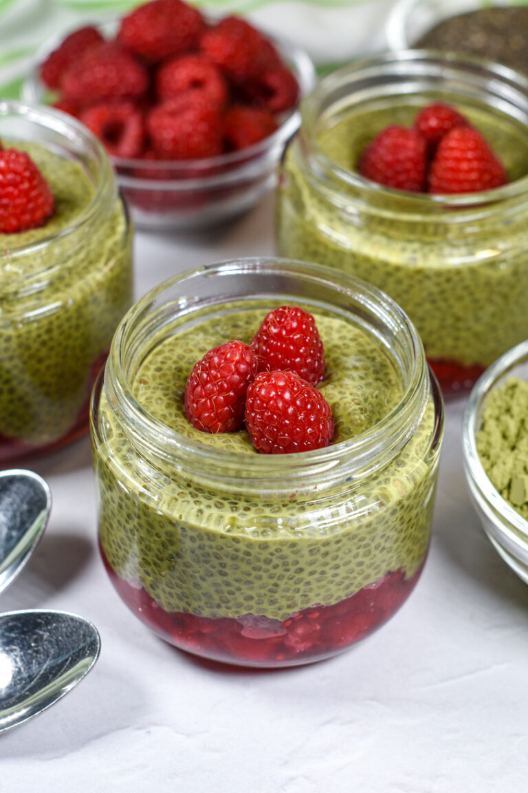 glass jar of matcha pudding garnished with fresh raspberries