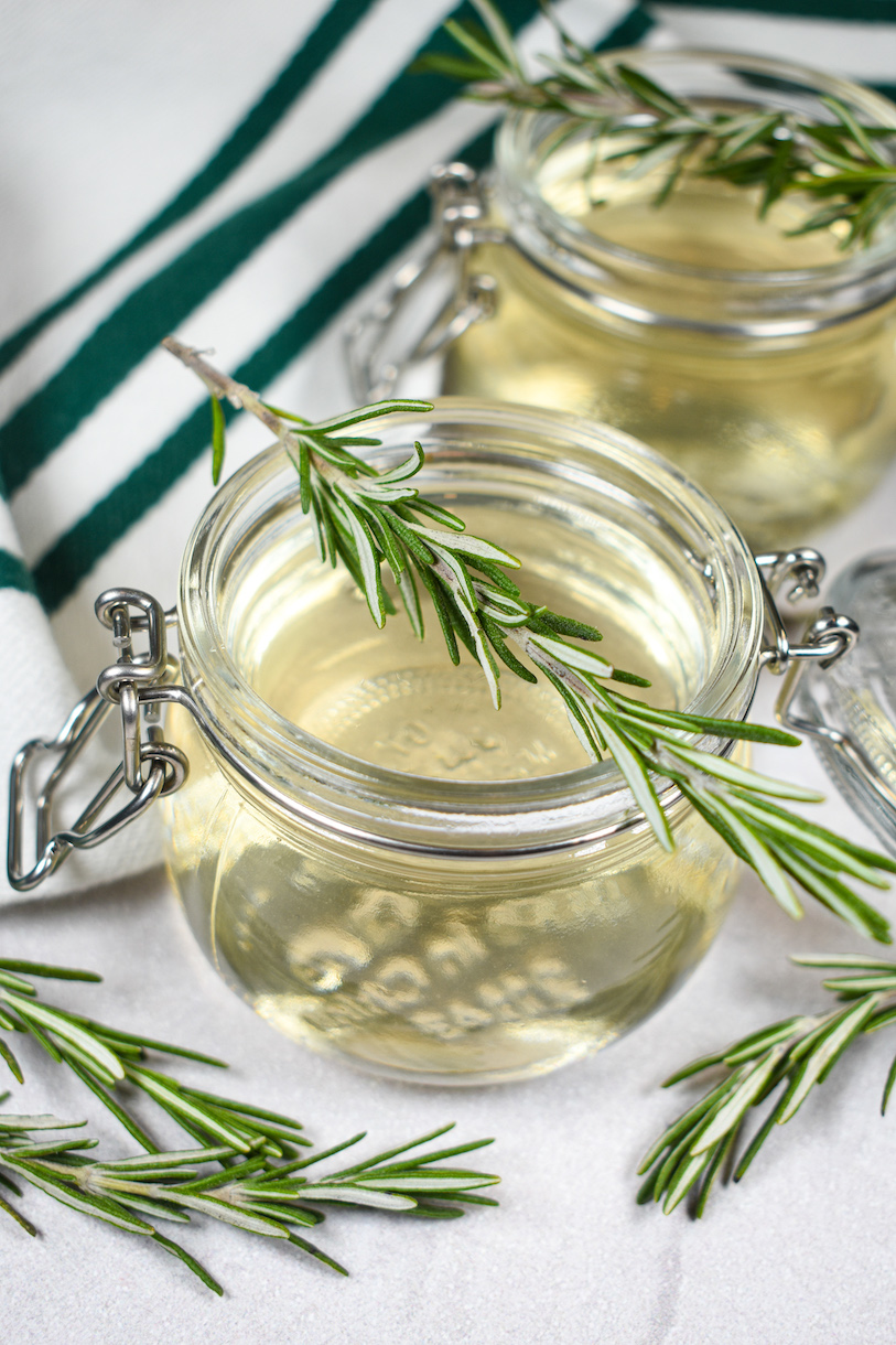 Glass jars of rosemary infused simple syrup with sprigs of fresh rosemary on top