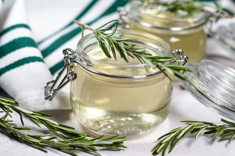 a jar of rosemary syrup with a sprig of fresh rosemary on top