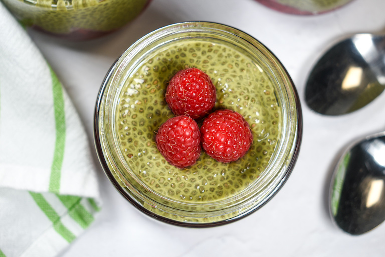 Looking down at a jar of matcha chia pudding garnished with three raspberries