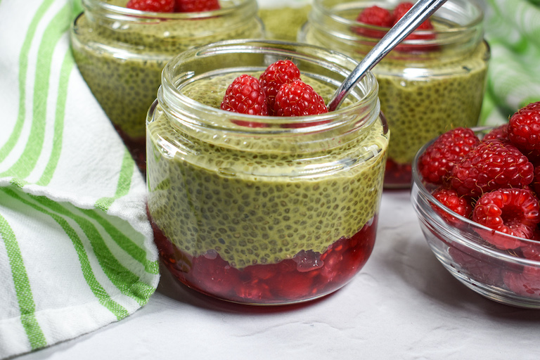 A jar of layered raspberry and matcha chia pudding with a spoon