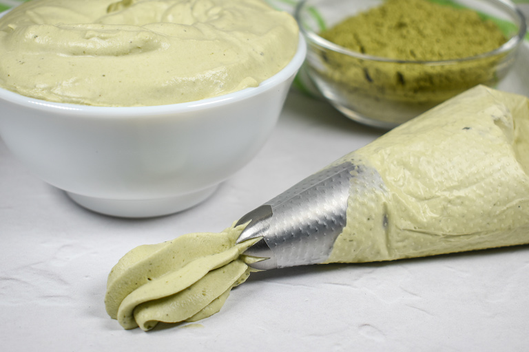 A piping bag of matcha whipped cream with a dish of matcha in the background