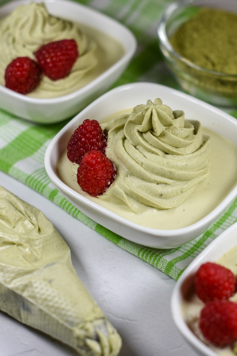 Dishes of matcha pudding with matcha whipped cream and raspberries on top