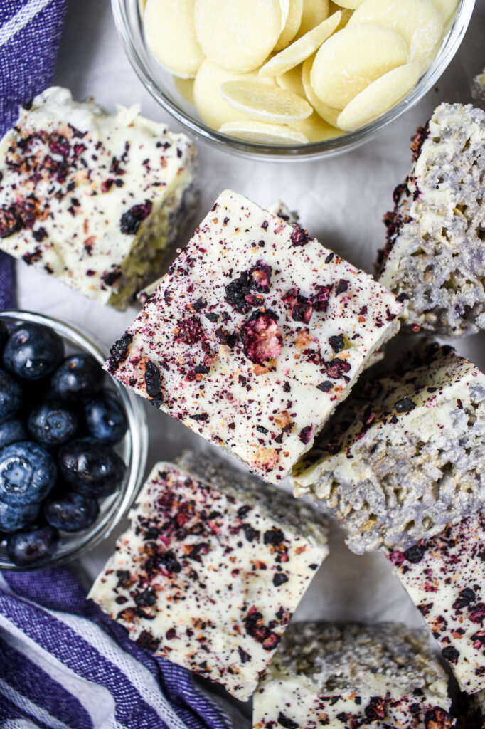 Vertical shot of blueberry krispie treats, dish of blueberries, and dish of white chocolate callets
