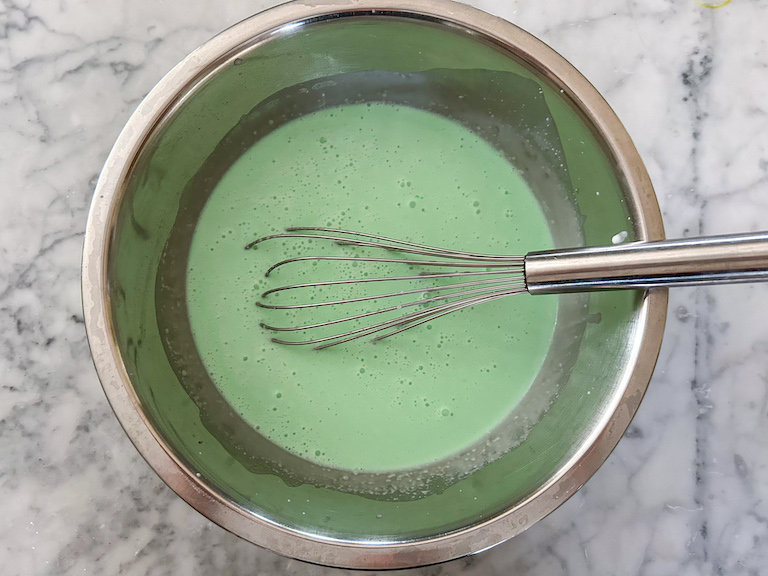 Mint chocolate chip ice cream base in a bowl with a whisk