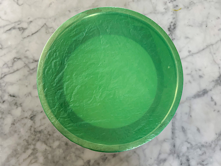 Mint chocolate chip ice cream base in a bowl covered with green plastic