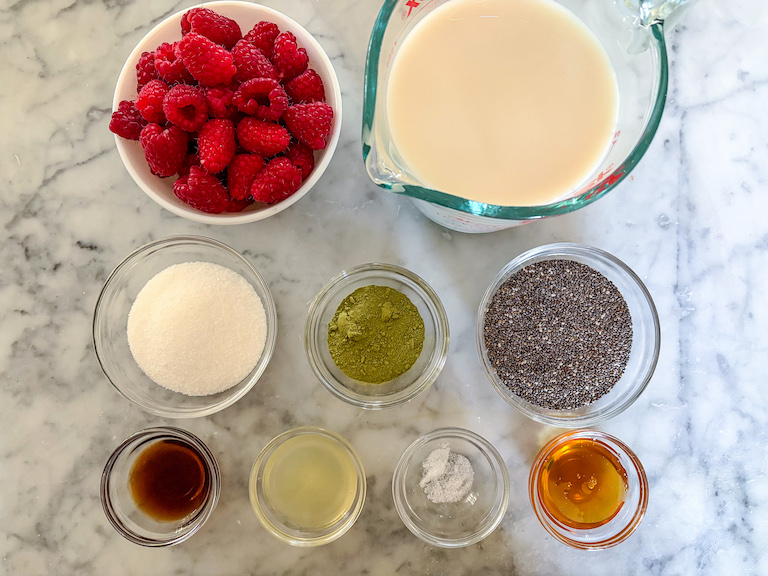 Ingredients for making raspberry matcha chia seed pudding arranged on a marble surface