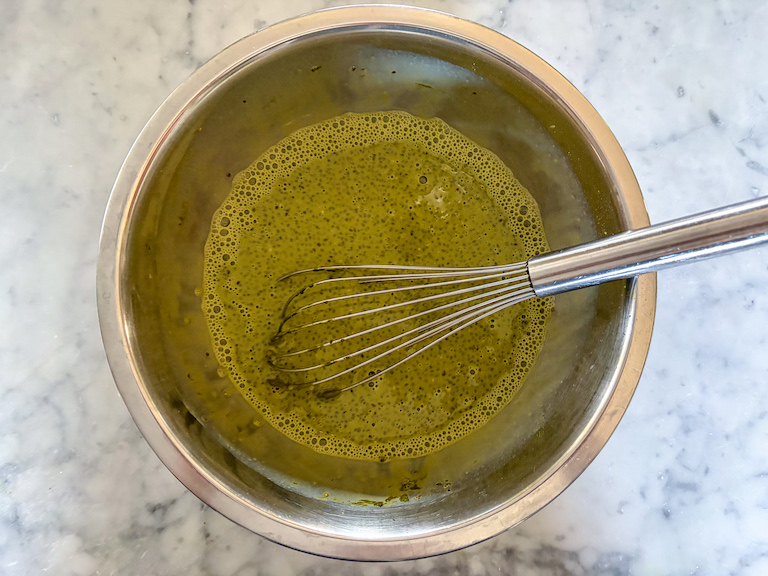 Whisking matcha pudding ingredients in a metal bowl