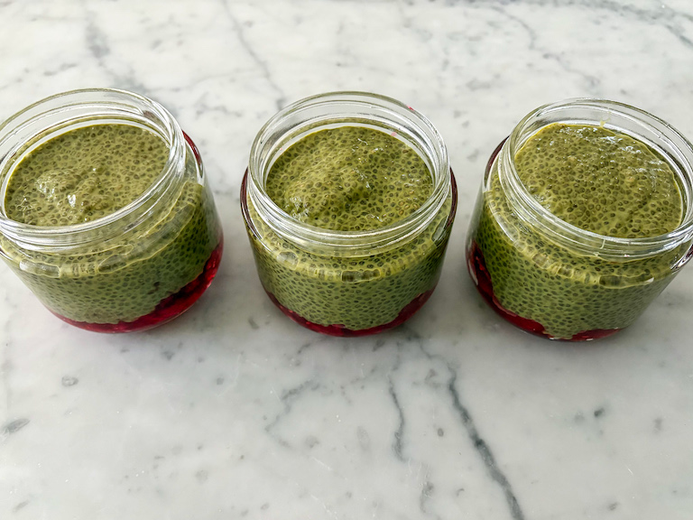 Three jars of matcha raspberry chia seed pudding on a marble surface