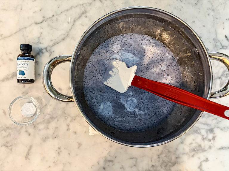 Melted blueberry marshmallows in a pot next to a dish of sea salt and bottle of blueberry flavoring