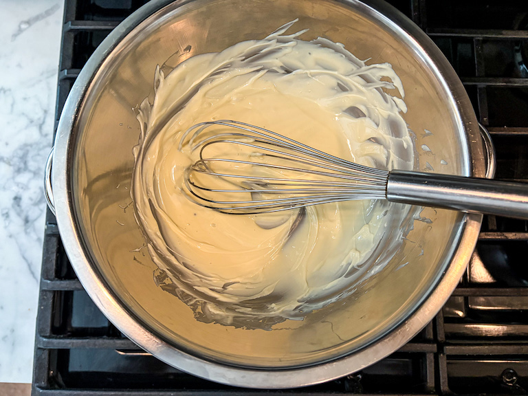 melted white chocolate in a mixing bowl with a whisk