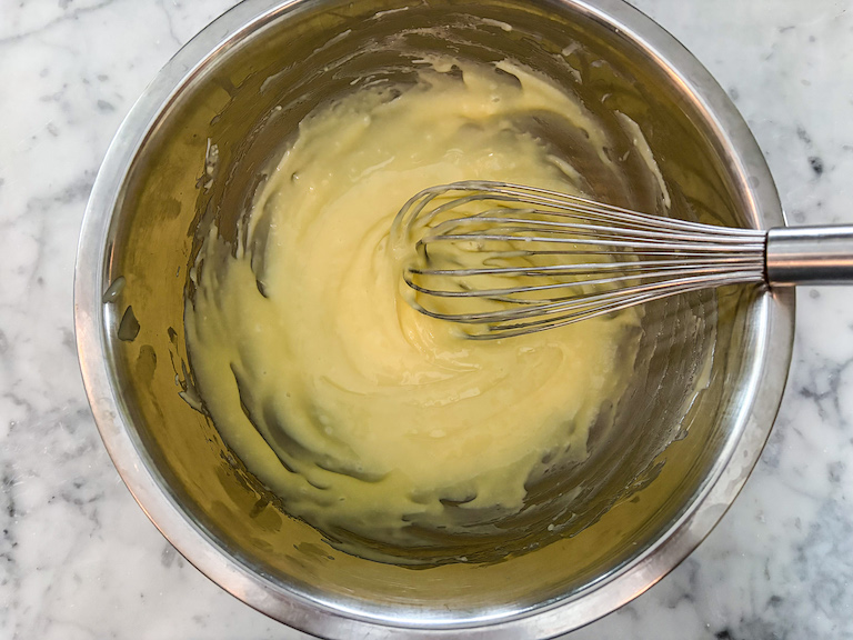 A bowl of white chocolate ganache with a whisk