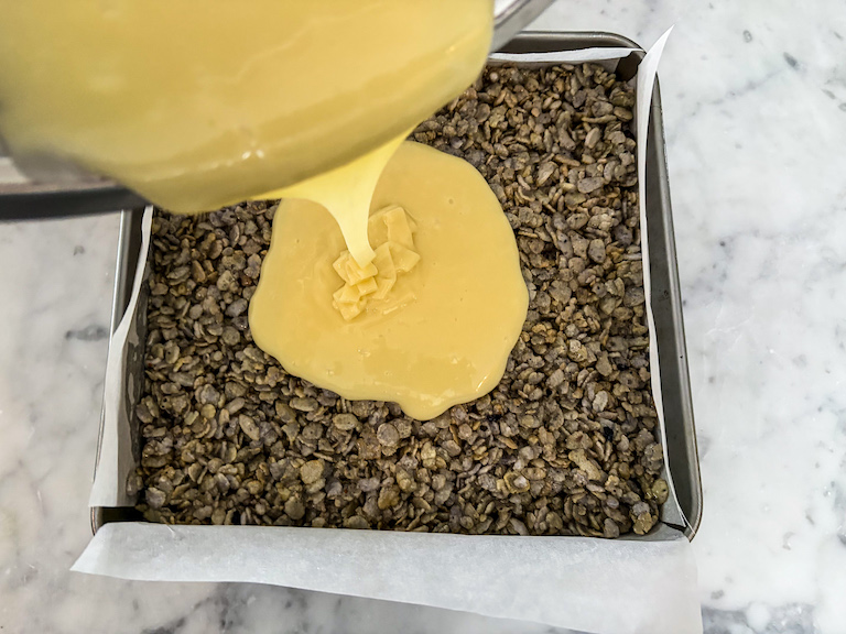 Pouring white chocolate ganache over a pan of blueberry cereal treats