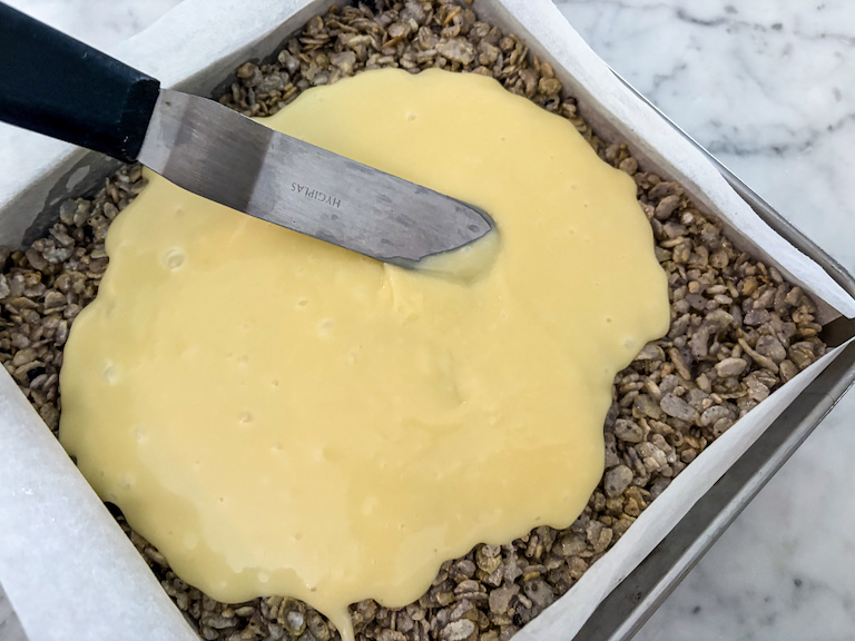 Palette knife spreading white chocolate ganache over cereal treats