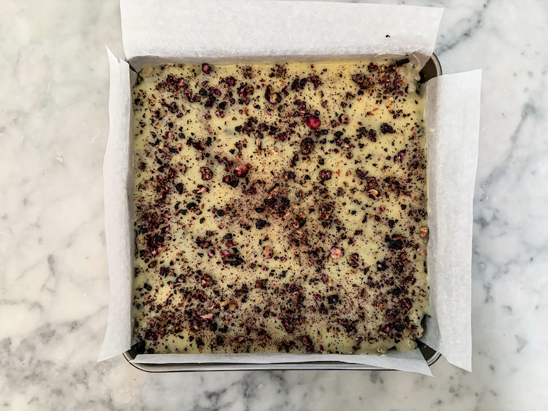 A pan of blueberry rice krispie treats with white chocolate ganache and crushed freeze dried berries on top