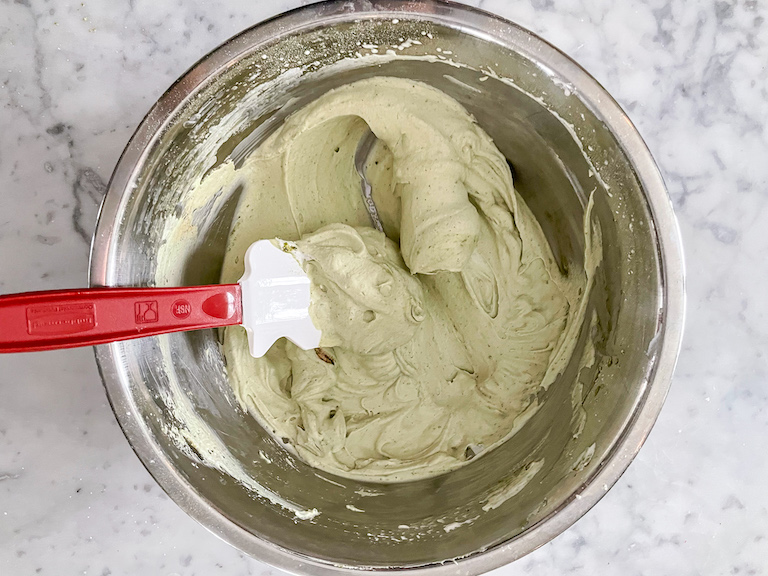 A bowl of matcha whipped cream with a rubber spatula