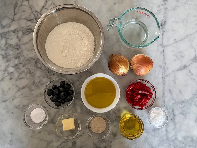 Ingredients for making caramelized onion focaccia arranged on a marble surface