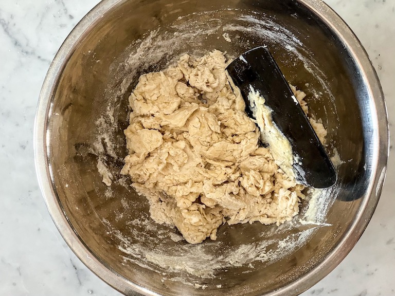 Focaccia dough in a bowl with a bench scraper