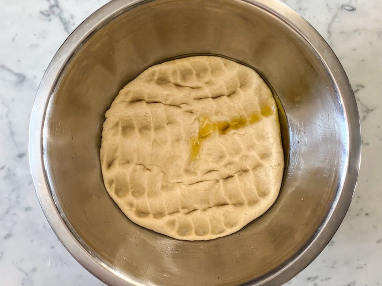 Punched-down bread dough in a metal bowl