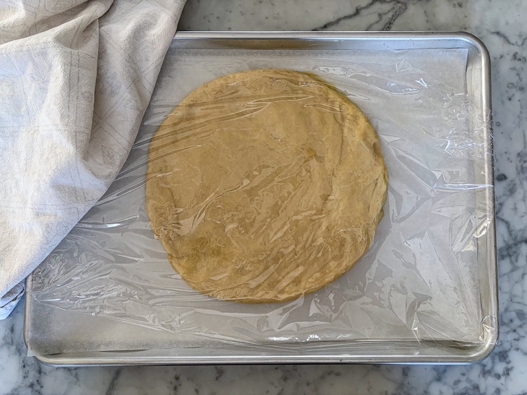 A tray with a round of bread dough, covered in plastic wrap