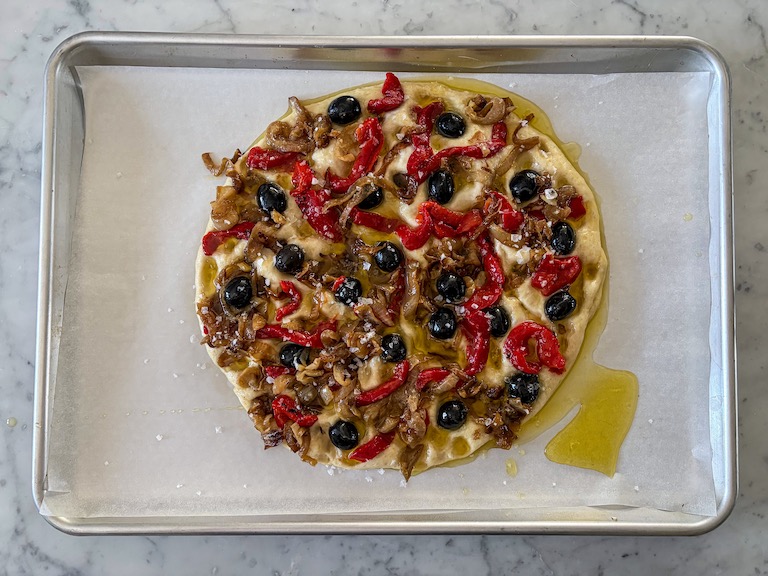 Focaccia dough decorated with onions, peppers, olives, and olive oil