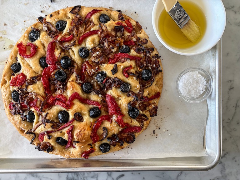 Focaccia on a tray with a dish of olive oil and dish of sea salt