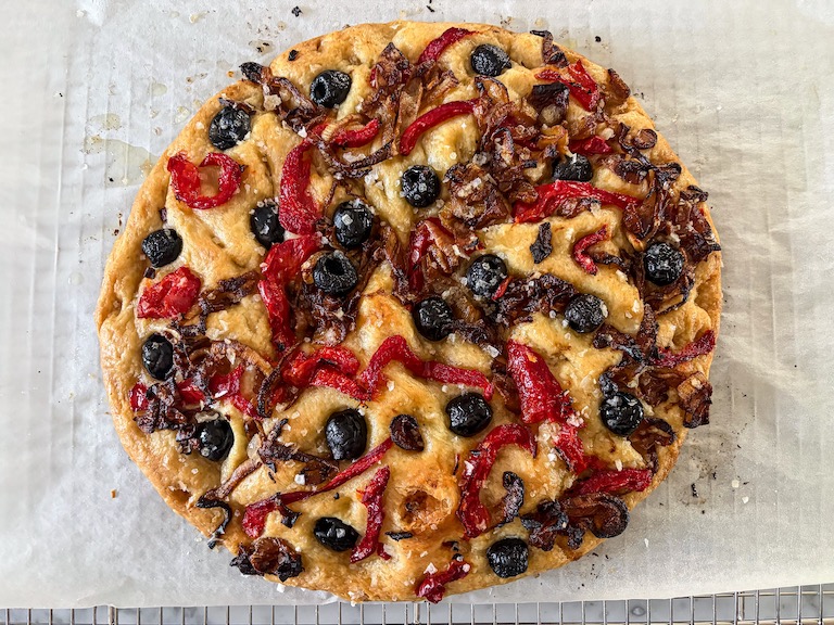 A loaf of caramelized onion and roasted red pepper focaccia on a sheet of parchment