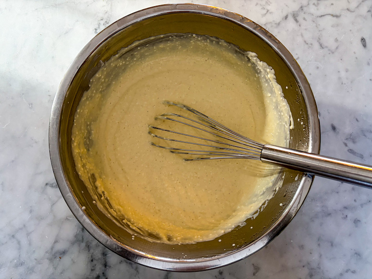 Cheesecake ice cream base in a bowl with a wire whisk