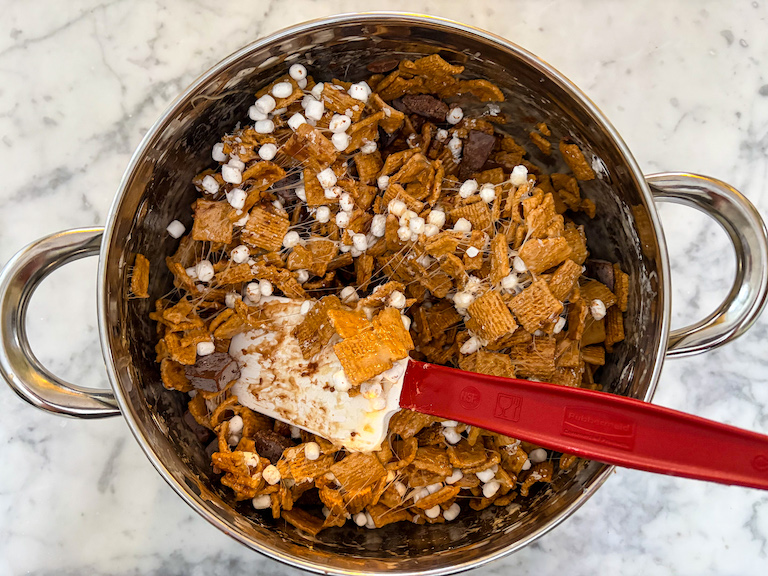 Spatula stirring together marshmallows, graham cereal, and chocolate