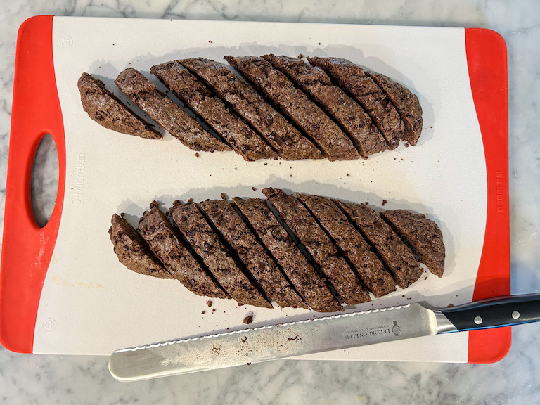 Slices of biscotti and a serrated knife on a cutting board