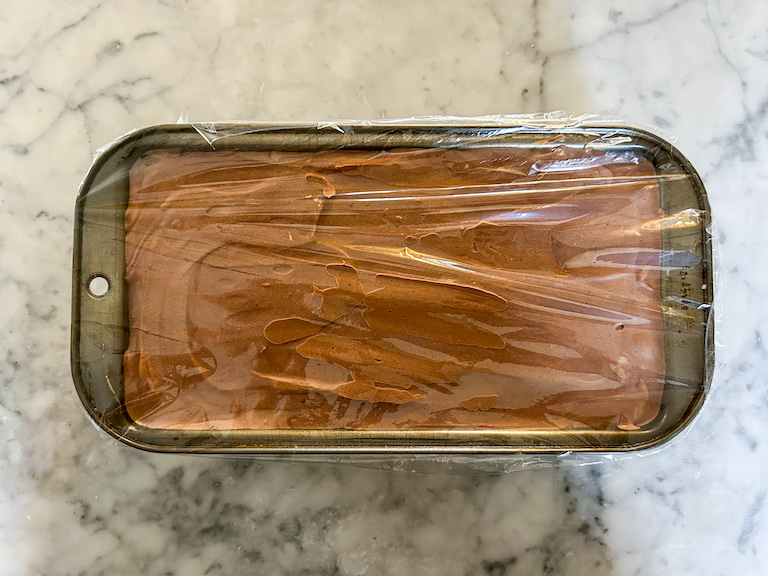 Loaf pan of chocolate ice cream covered with plastic wrap