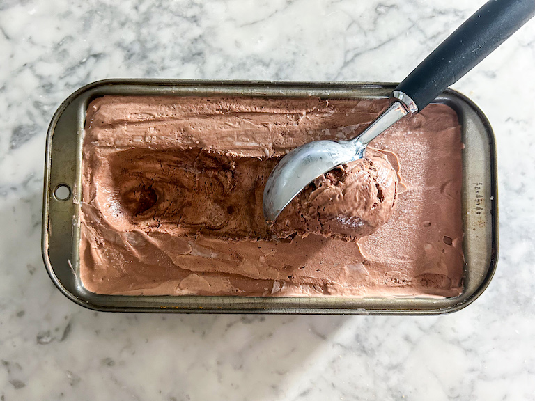A loaf pan of chocolate ice cream with an ice cream scoop