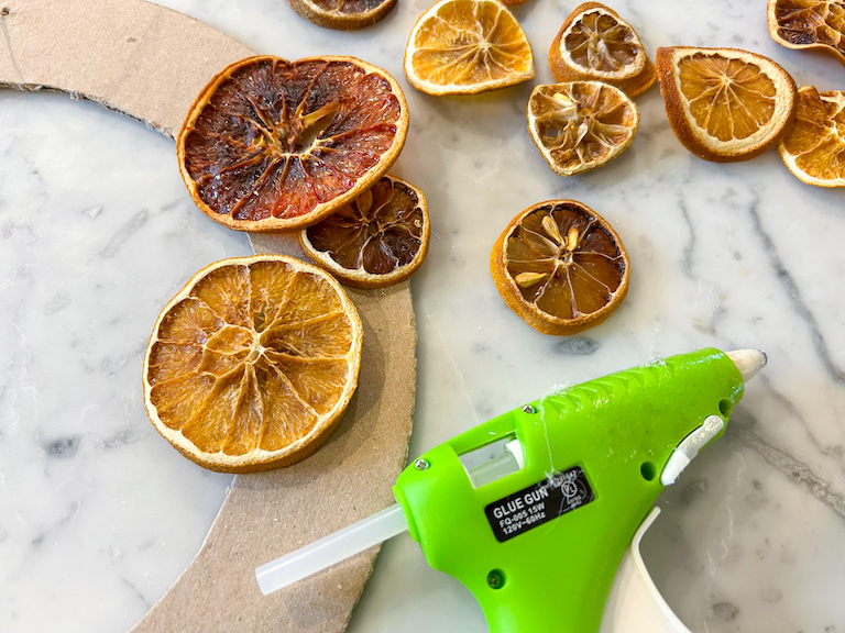 Hot glue gun attaching dried citrus slices to a cardboard ring