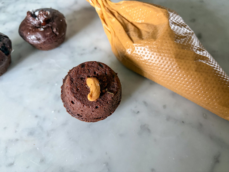 Mini muffin filled with peanut butter next to a piping bag of peanut butter