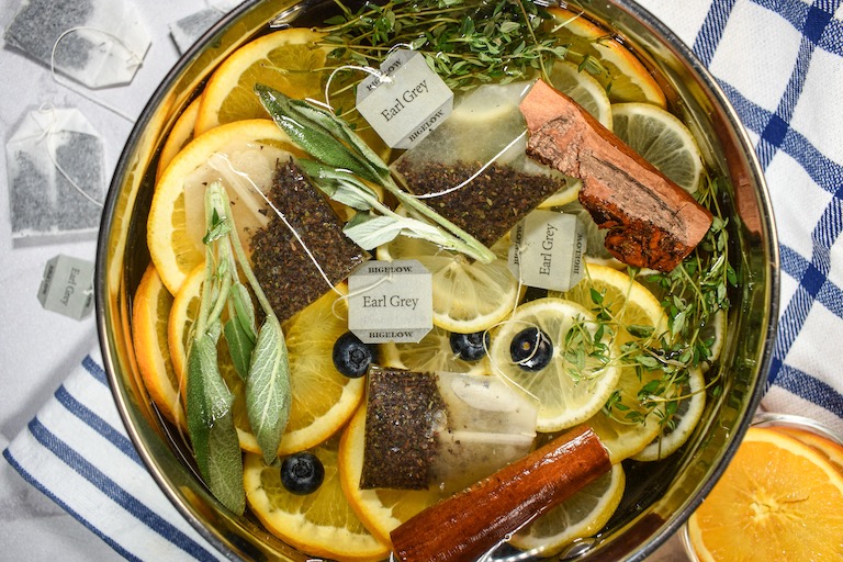 An Earl grey simmer pot surrounded by tea bags and dishes of sliced citrus fruit
