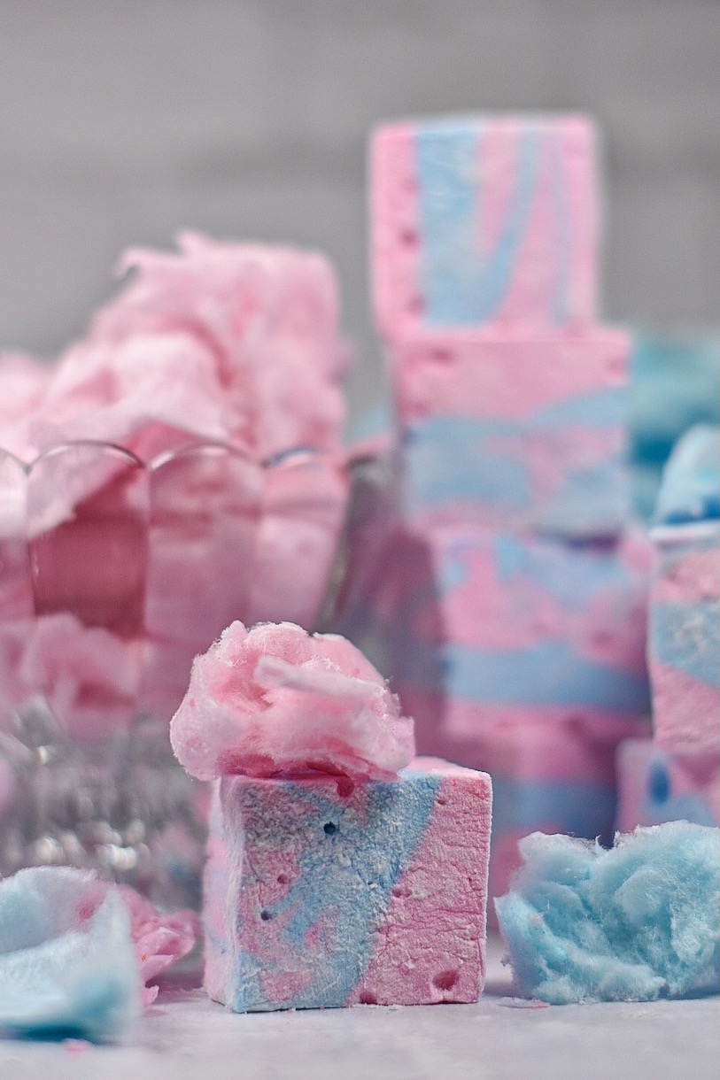 Pink and blue cotton candy marshmallows and puffs of spun sugar on a white surface