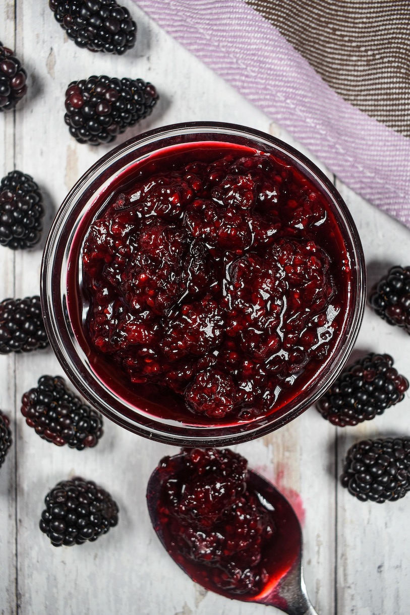 A dish of blackberry compote, spoon, and fresh berries