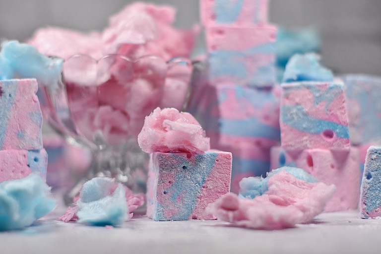 Pink and blue cotton candy marshmallows and puffs of spun sugar on a white surface