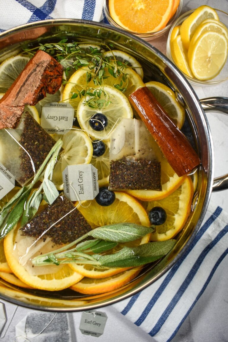 Earl Grey simmer pot arranged on a white surface with striped towels and dishes of citrus fruit