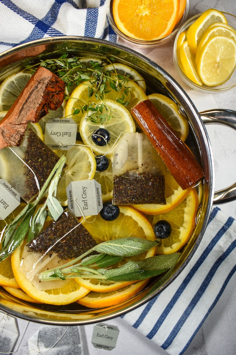 Horizontal shot of an Earl Grey simmer pot surrounded by tea bags dishes of fresh citrus